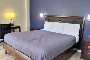 A bed with a patterned bedspread, a wooden headboard, two bedside tables, and wall-mounted lights.
