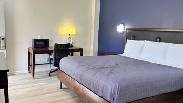 Een hotelkamer met een bed, een bureau met een computer, een lamp en een magnetron.