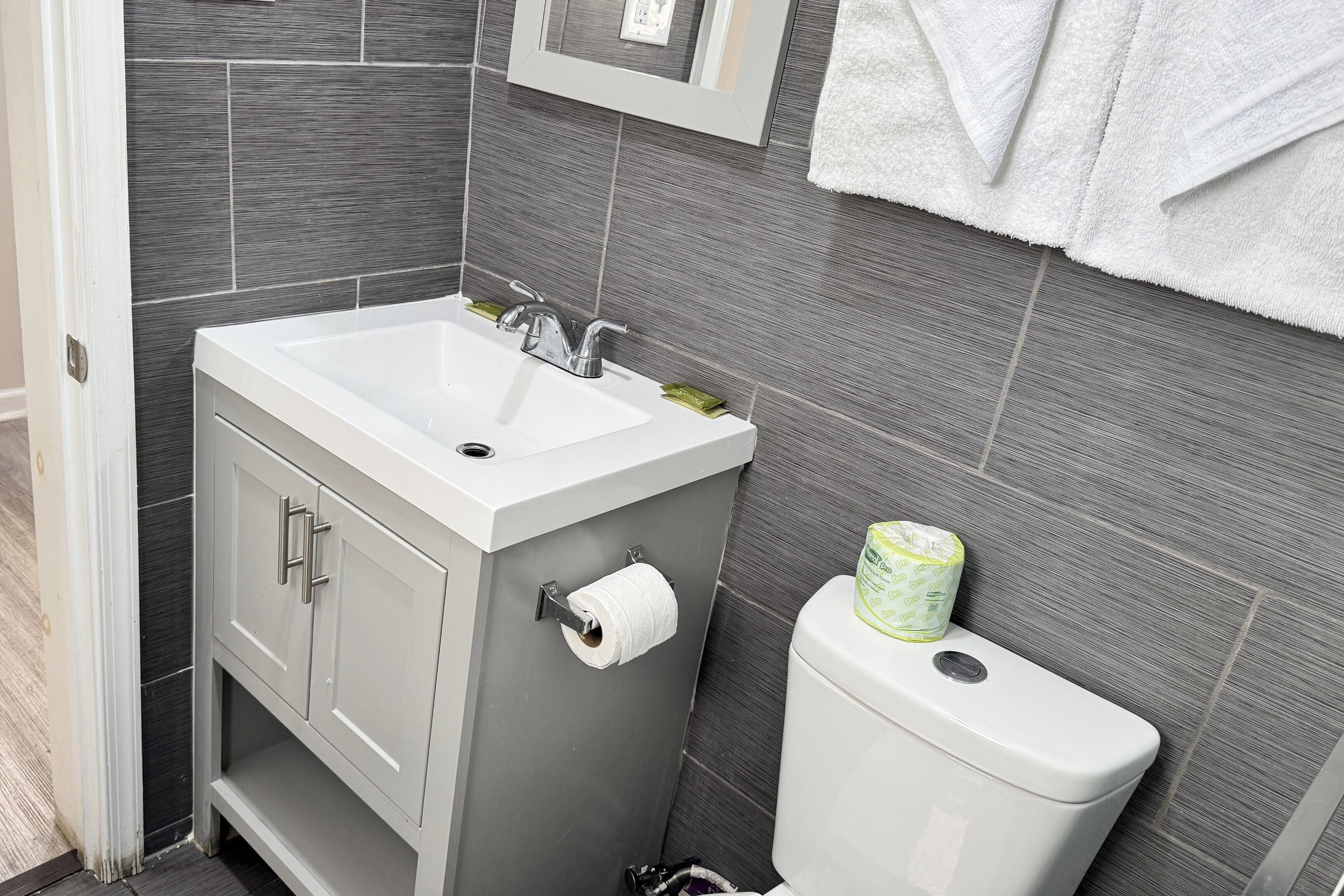 A bathroom with a white sink, a toilet, and grey tiled walls.