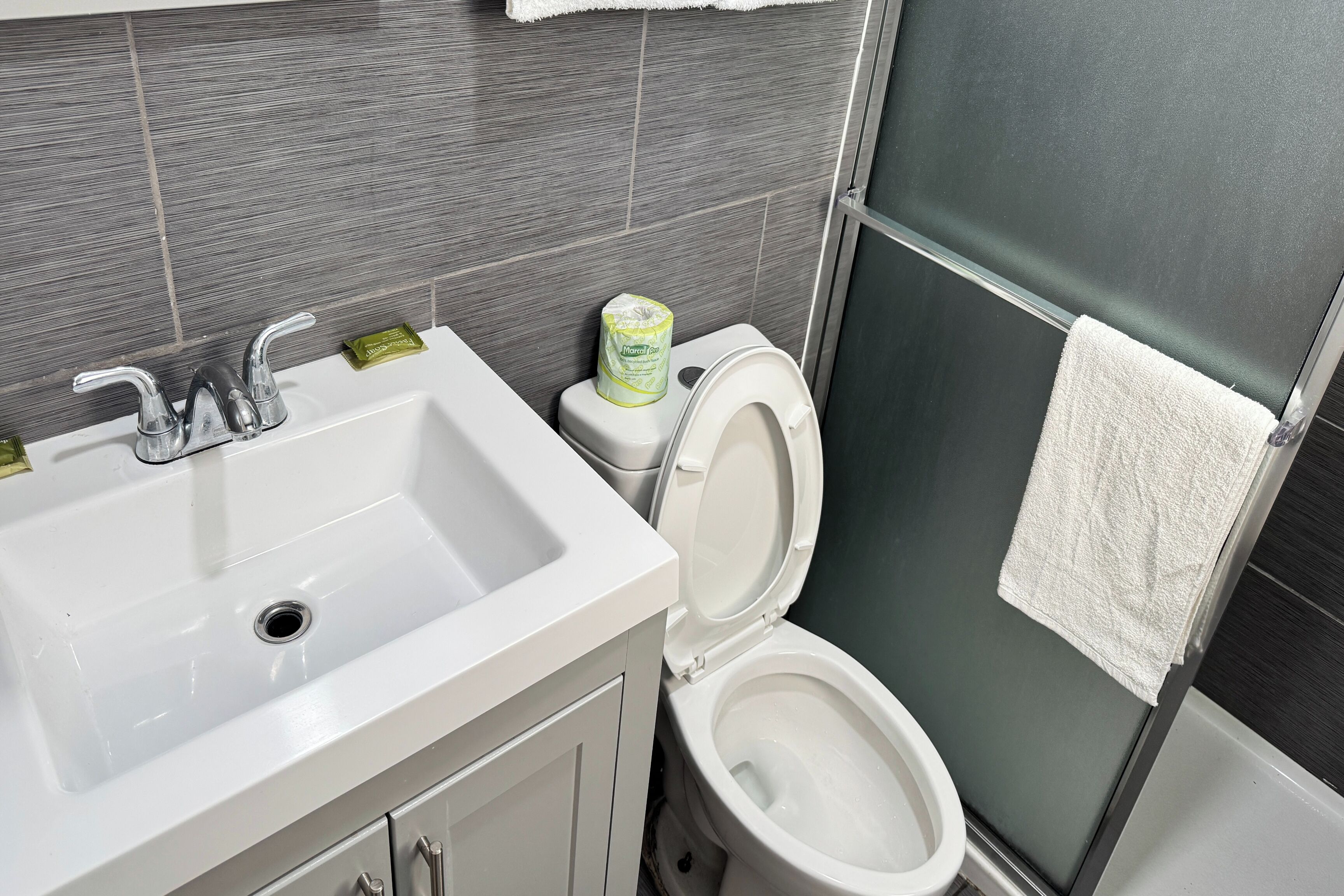 A bathroom with a white sink, two faucets, a toilet, and a glass shower enclosure.