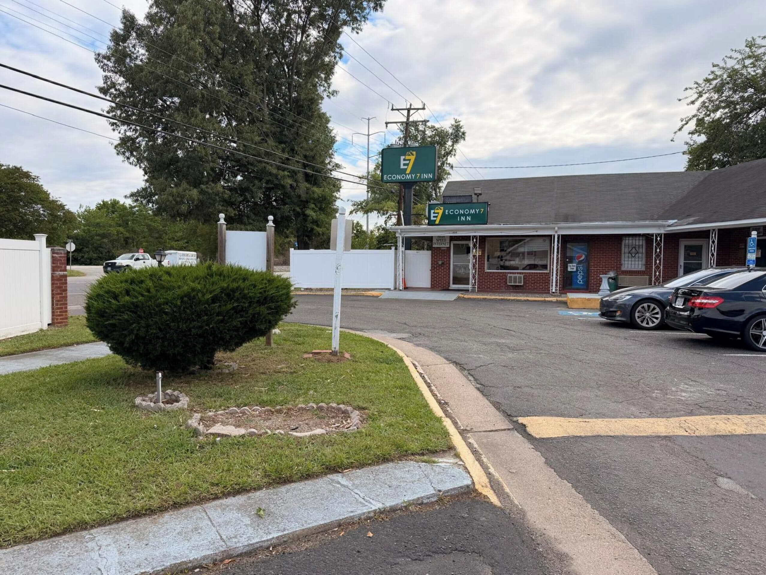 A Economy 7 Inn with a brick facade, a signboard, and a parking lot with cars.