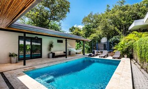 Ein moderner Poolbereich mit klarem, blauem Pool, Liegestühlen und einer überdachten Lounge.
