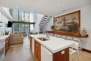Enjoy cooking in the central island kitchen with a sink and bar stools, opening up to a living area with a sofa and staircase.