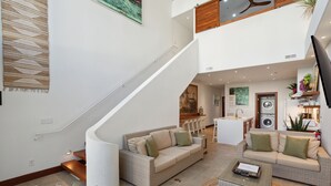 A spacious living area with a high ceiling, a staircase, and a kitchen in the background. - Vacation Villa 5 mins to King ‘The Royal Palm’ (Charleston)