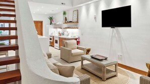 Un vaste espace de vie doté d’un haut plafond, d’un escalier, d’un téléviseur à écran plat fixé au mur et d’une cuisine à l’arrière-plan.