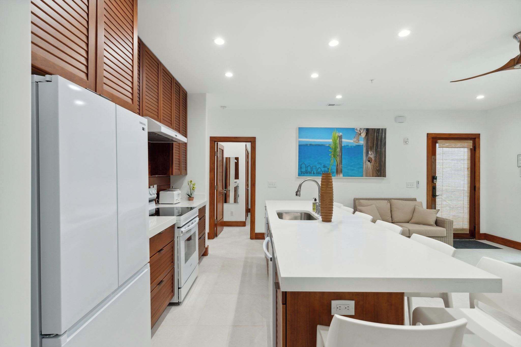 A modern kitchen with a central island, wooden cabinets, and a large refrigerator.