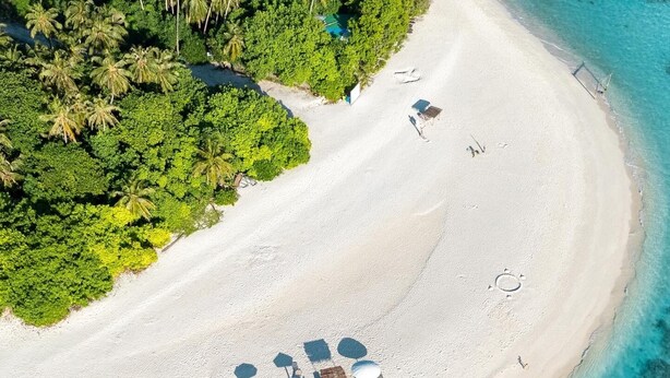 An aerial view of a beach with clear turquoise waters, a sandy shore, and a small cluster of umbrellas and lounge chairs. - Odi Kamadhoo (Kamadhoo)