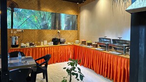 A breakfast buffet setup with a large window, a fan, and a plant. - Odi Kamadhoo (Kamadhoo)