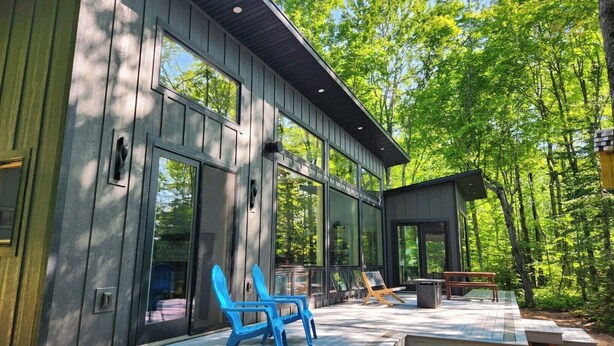 A modern cabin with large windows, a deck with outdoor seating, and a forested backdrop.