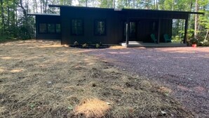 A modern cabin with a covered porch, surrounded by a forest.