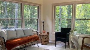 A spacious room with large windows, a wooden floor, a sofa, a chair, and a rug.