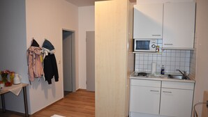 Una stanza funzionale con un letto, un tavolino con un vaso e un bollitore, un forno a microonde e un lavandino.