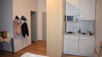 Ein kleines Zimmer mit einem Bett, einem kleinen Tisch mit einer Vase und einem Wasserkocher, einer Mikrowelle und einem Waschbecken.