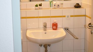 Un bagno con lavandino bianco, specchio e pareti piastrellate. Sul mobile ci sono articoli da toilette e un cestino sotto il lavandino.