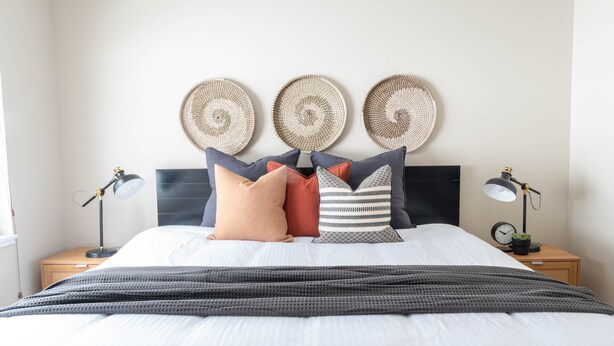 Un lit bien fait, recouvert d’une couverture à rayures, trois éléments de décoration murale et deux tables de chevet avec des lampes.