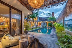 A modern outdoor pool area with wooden decking, lounge chairs, and a thatched roof structure. - NEW Listing! 4BR Tropical Private Villa in Umalas (Kerobokan)