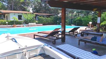 Un espace aménagé au bord de la piscine, avec des chaises longues, un coin salon abrité et un bateau amarré au bord du bassin.