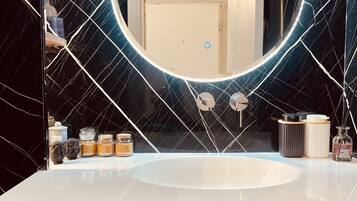 A bathroom with a white sink, a round mirror with a light, and a door in the background.