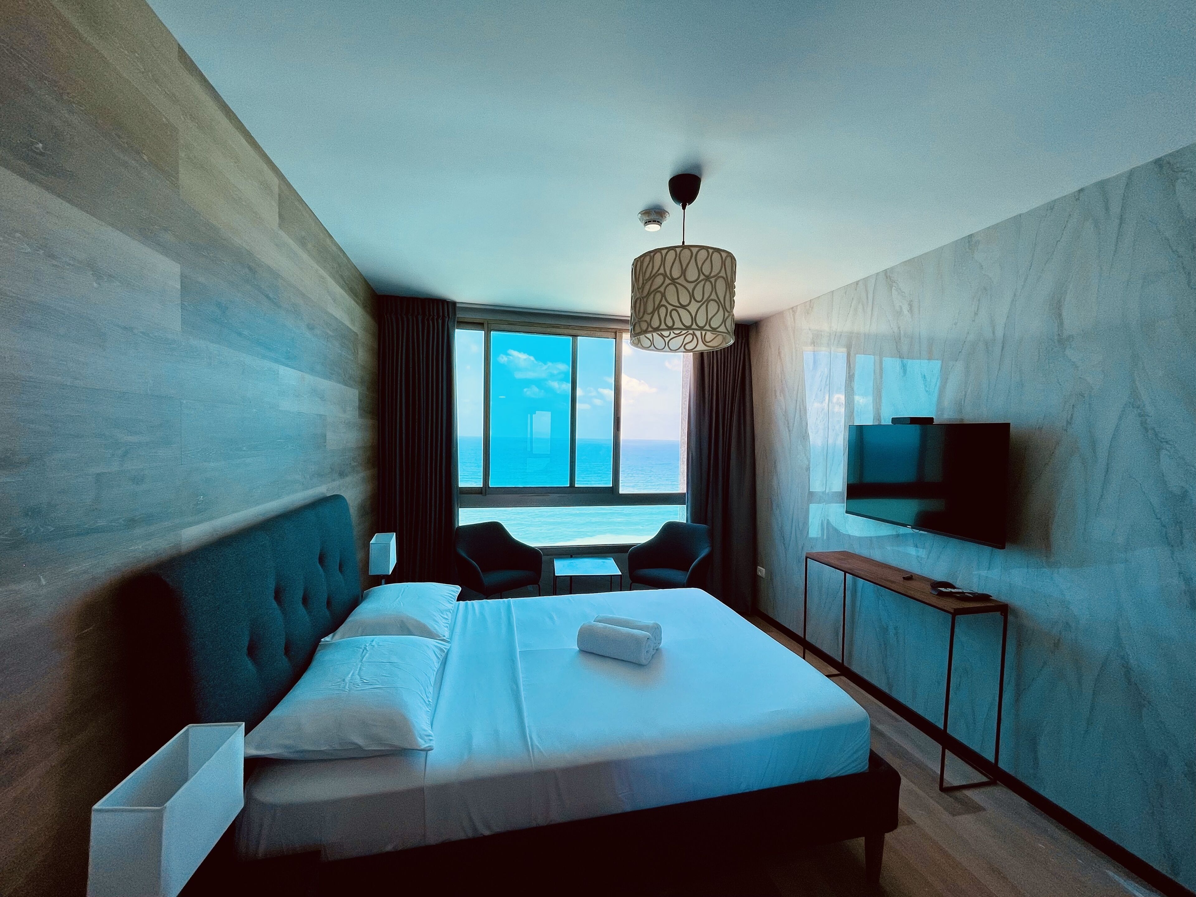 Une chambre d’hôtel moderne avec un grand lit, une télévision et une vue sur la mer.