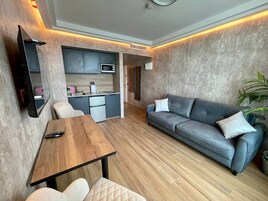 Un espacio habitable compacto con kitchenette, un sofá, una mesa de comedor y un televisor montado en la pared.