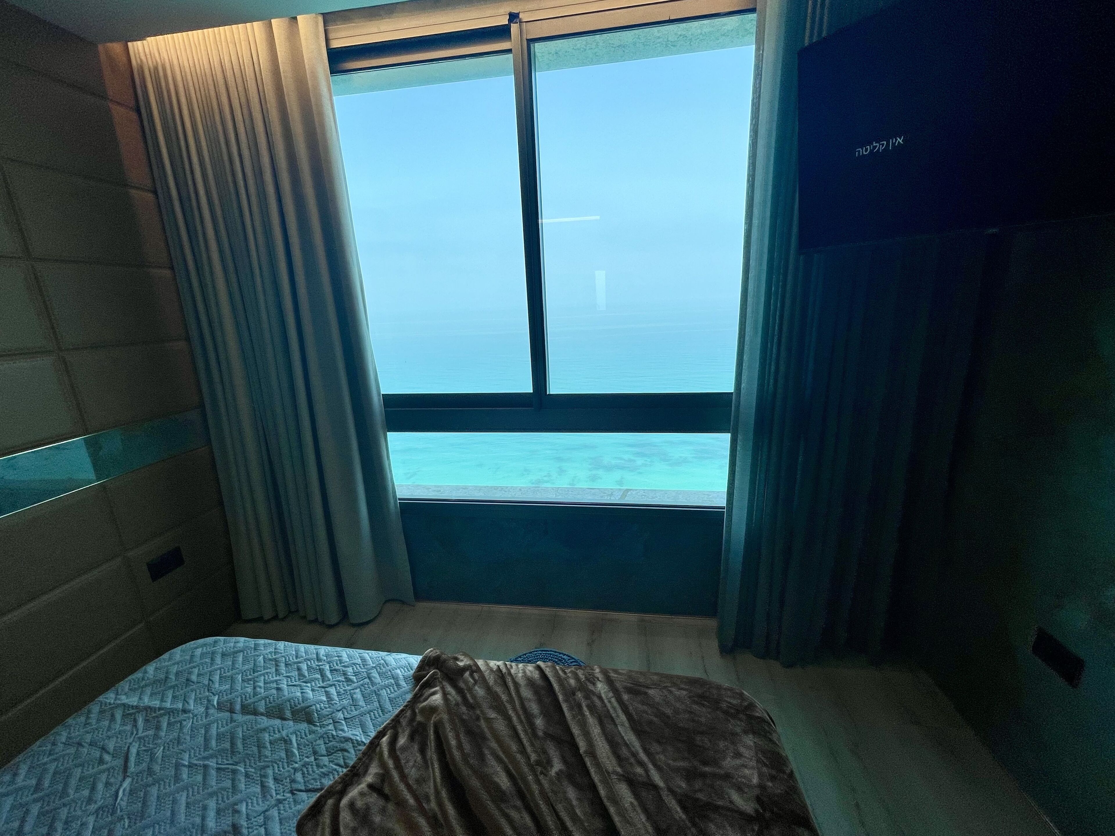 Habitació d'hotel amb un llit, vistes al mar i cortines.
