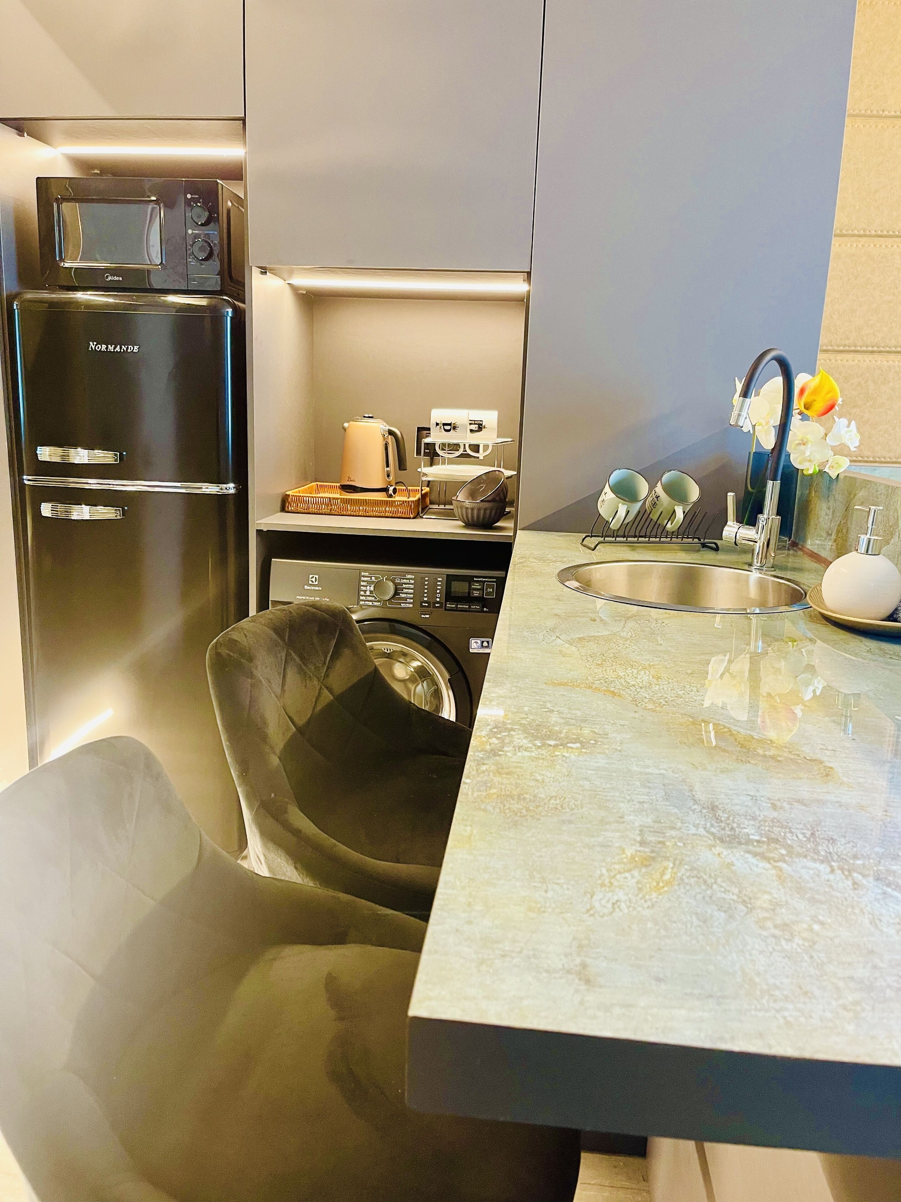 Una cucina compatta con lavatrice, forno a microonde e lavello dotato di un rubinetto moderno.