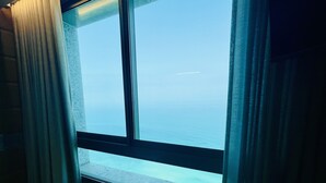 A window with a view of the sea, curtains, and a concrete ledge. - Carmel Holiday Apartments (Netanya)