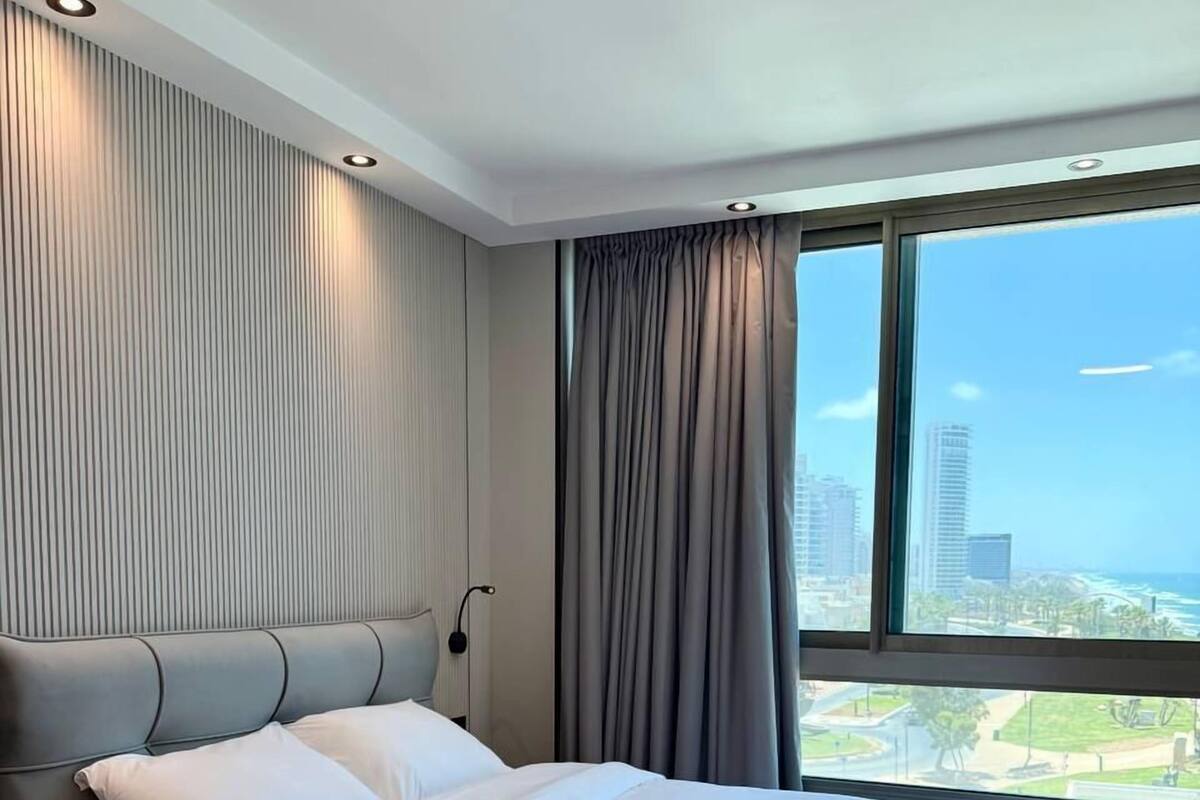 A modern hotel room with a large bed, a view of the cityscape, and a city skyline visible through the window.