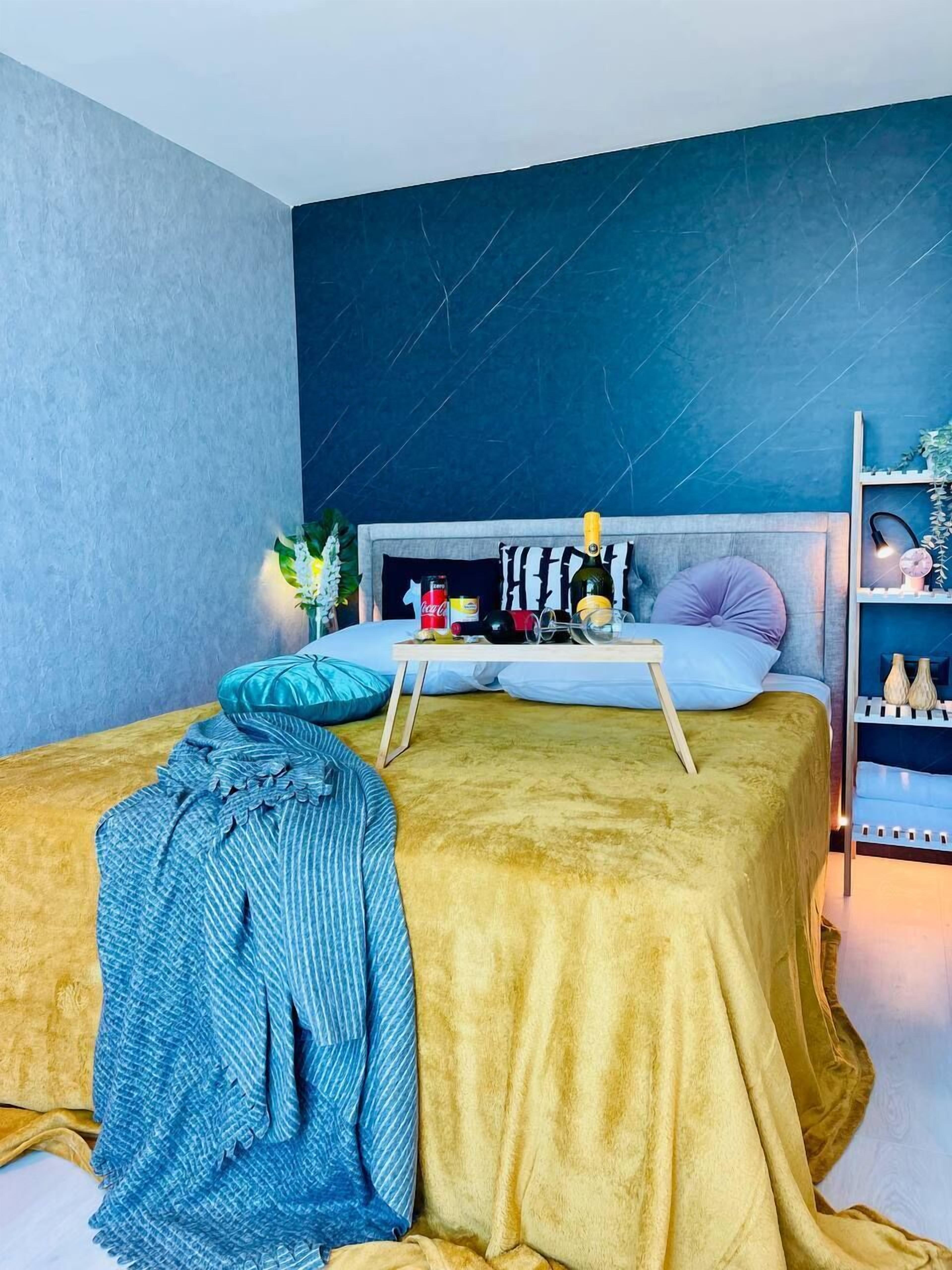 A bedroom with a bed, a bedside table, and a shelf with decorative items.