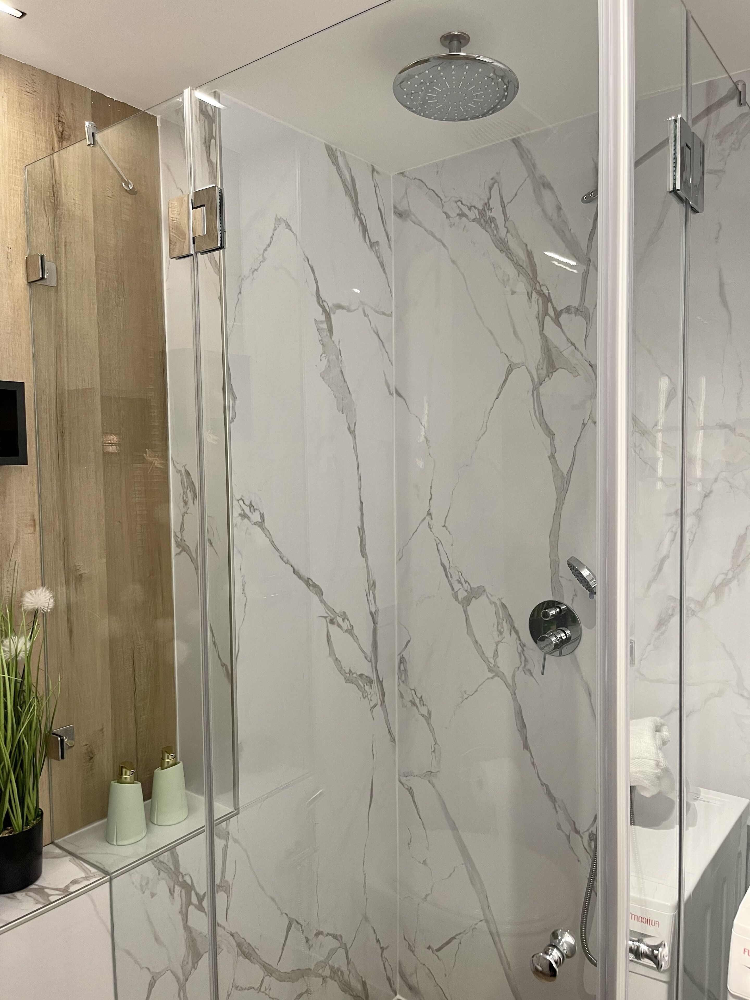 Un baño moderno con ducha de vidrio, paredes de mármol y una pared de acento de madera.