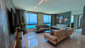 A modern living room with a large window, a flat-screen TV mounted on the wall, and a wooden coffee table.