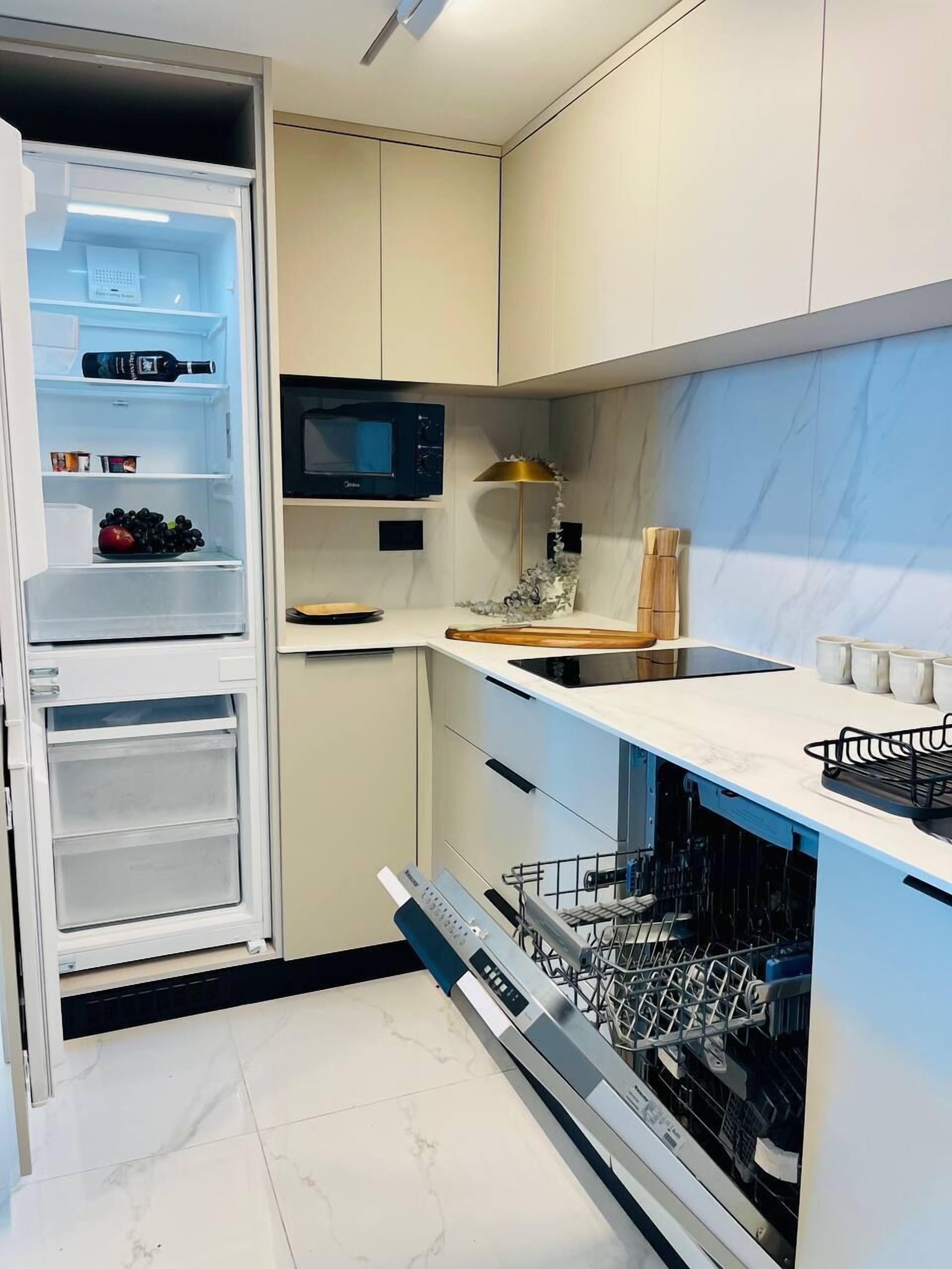 Une cuisine moderne équipée d’un four à micro-ondes encastré, d’un lave-vaisselle et d’une bouteille de vin dans le réfrigérateur.