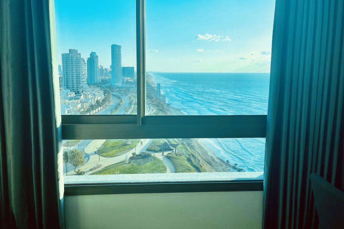 A view from a window overlooking a coastal cityscape with high-rise buildings and a beach.