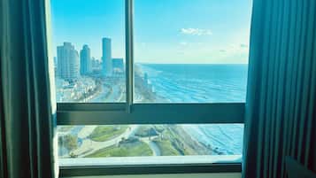 Vista desde una ventana que muestra un paisaje urbano costero con rascacielos y una playa.