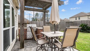 An outdoor patio with a grill, dining table, and chairs.