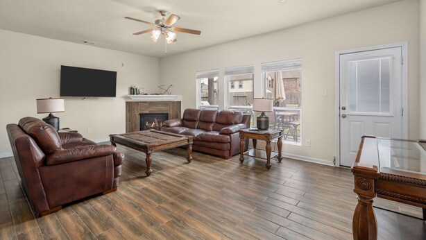 A living room with a brown leather sofa, a wooden coffee table, a fireplace, a ceiling fan, and a large window with blinds.