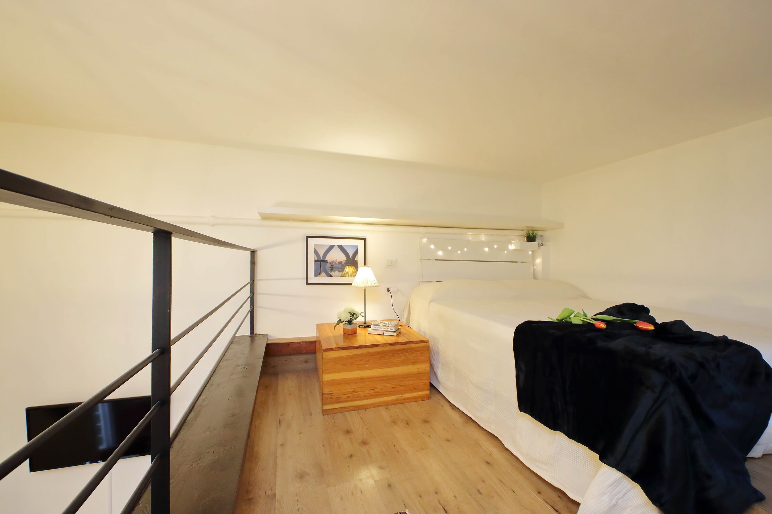 Une chambre à coucher avec un lit, une table de chevet avec une lampe, un tableau au mur et un escalier.