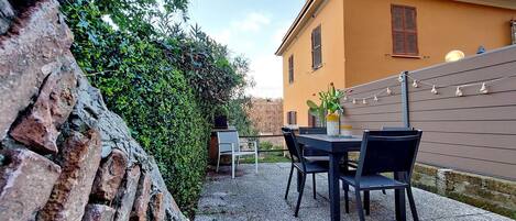 A patio with a table and chairs, a brick wall, and a building with a yellow facade.