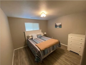 Une chambre à coucher comprenant un lit, une table de chevet, une commode, une fenêtre et un luminaire au plafond.