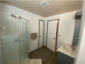 A modern bathroom with a glass shower enclosure, a wooden floor, a white sink with a mirror, and a towel rack.