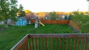 A backyard with a wooden deck, a play structure, and a fenced area. - 5 Bedroom Home for your Black Hills Adventures (Rapid City)