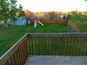 Enjoy a serene outdoor space with a deck, play structure, and shed surrounded by trees and a hill.