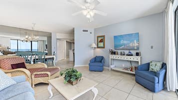 A spacious living room with a dining area, a ceiling fan, a large window, and a cityscape painting.