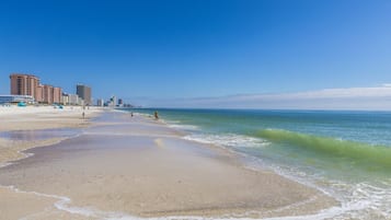 A beach with a sandy shore, a clear blue sky, and buildings in the background.