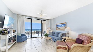 Amplia sala de estar con balcón, televisión, sofá, mesa de centro y silla de mimbre.