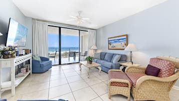 A spacious living room with a balcony, a television, a sofa, a coffee table, and a wicker chair.
