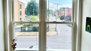 Una ventana con vista a una calle y edificios, una barandilla metálica y un cable de electricidad.