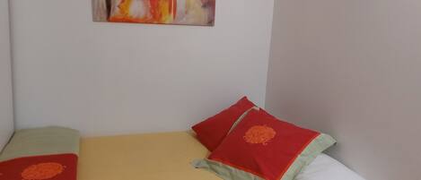 Une chambre avec un lit, un oreiller à motifs orange, un oreiller rouge et un tableau accroché au mur.