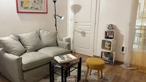Een woonkamer met een bank, een salontafel, een vloerlamp, een boekenkast en een deur.
