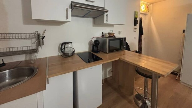 Een compacte keuken met witte kastjes, een roestvrijstalen spoelbak, een magnetron en een kleine koelkast.